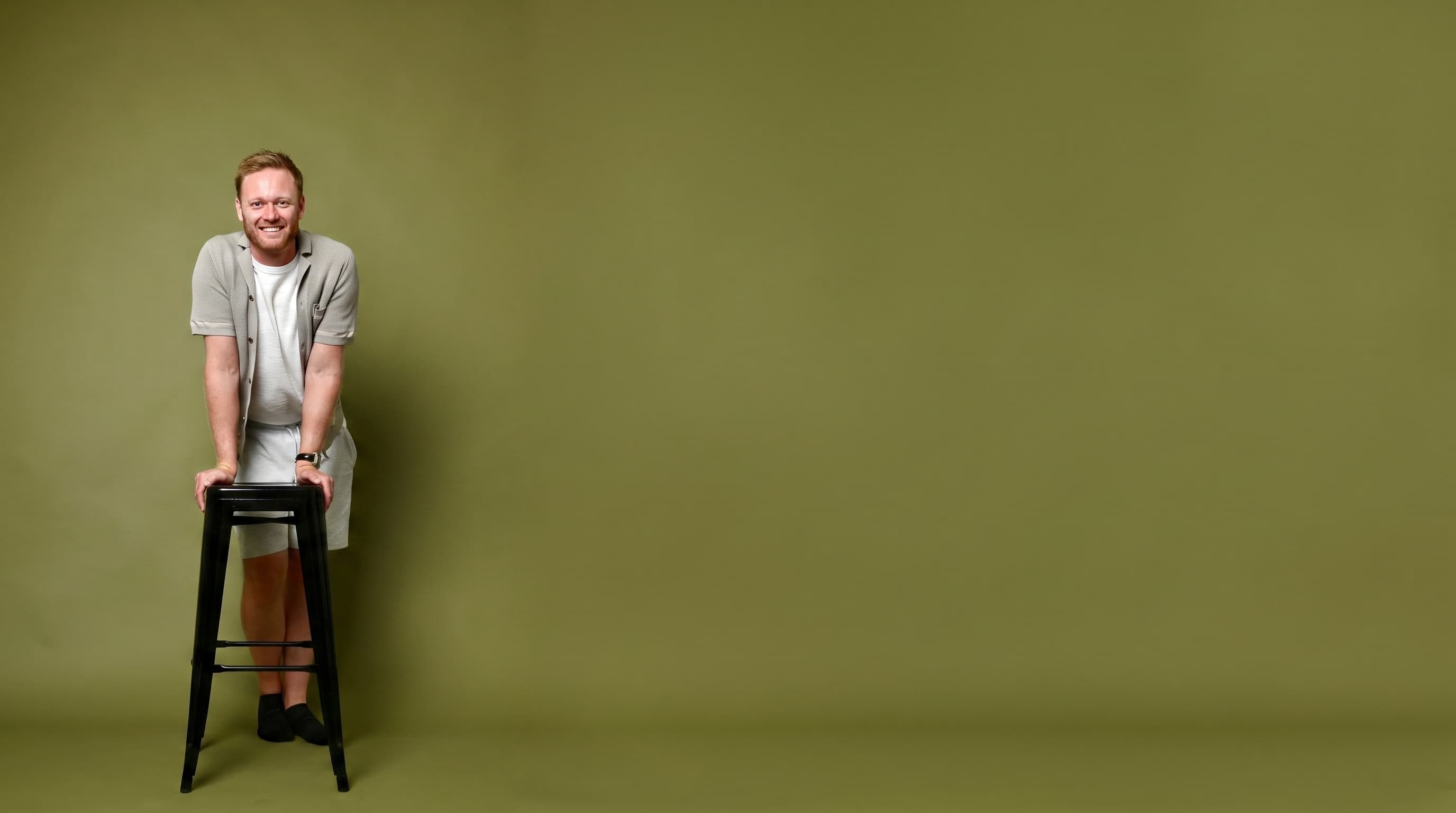 Terry Coopey leaning on a stool against an olive backdrop